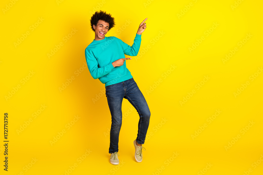Fototapeta premium Cheerful young man in teal sweatshirt posing against a vivid yellow background conveying positivity and enjoyment