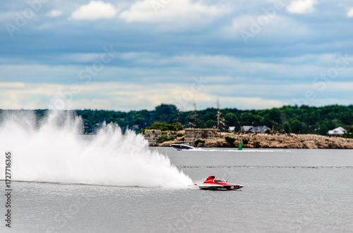 Red and white racing boat spraying a wake on a cloudy day