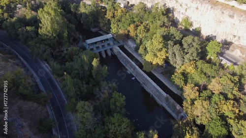 Aerial view of a hydroelectric power station in a small river surrounded by trees. Sustainable energy production from natural flowing water.