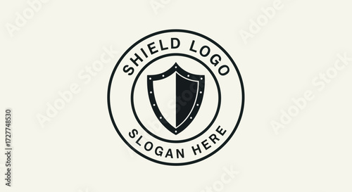 A circular emblem featuring a stylized shield divided into black and white halves, enclosed by text indicating "SHIELD LOGO" and "SLOGAN HERE" against a plain background.