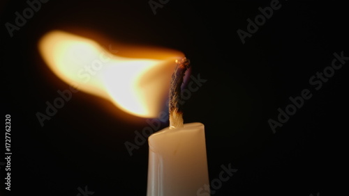 Fotografia Wind shaking candle flame in blackness closeup
