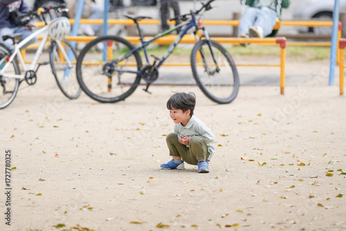 A young boy is playing in the park with a bicycle. The boy is crouching down and looking at something on the ground. The scene is peaceful and calm, with the boy enjoying his time outdoors