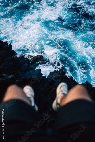 person sitting on a cliff with waves crashing against the cliff