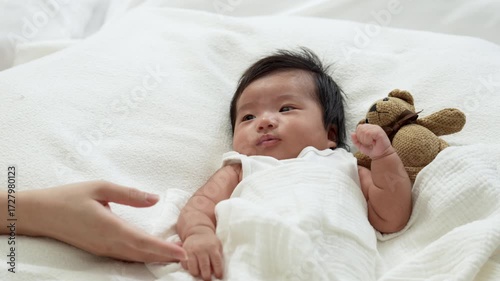 Mother hands play with her infant daughter laying on the white bed.