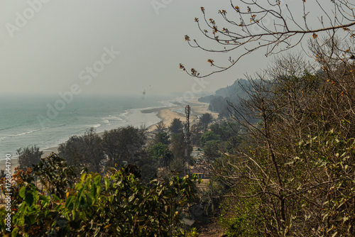 Peaceful panoramic scene of Cox’s Bazar Bangladesh coastline with glittering sea waves and forest trees on sandy beach.