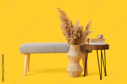 Soft bench with table, books and pampas grass in vase on yellow background
