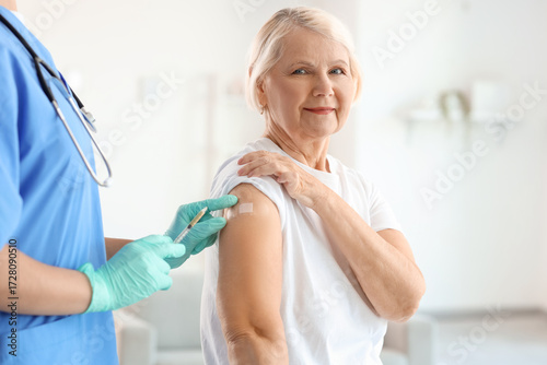 Obraz na plátne Senior woman receiving medical patch from doctor after vaccination at home