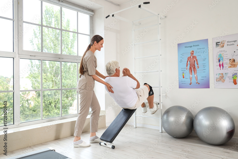 Fototapeta premium Female physical therapist assisting a senior man with abdominal exercises on an incline bench in a rehabilitation center