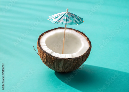 Half coconut with a cocktail umbrella on turquoise background
