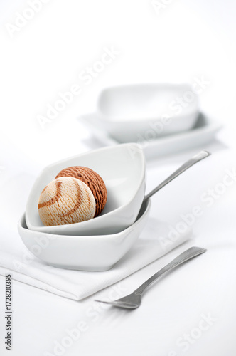 A scoop of ice cream served in a white bowl. A casually placed white bowls on a white background with chocolate ice cream. Beautiful and uncluttered dessert food photography.