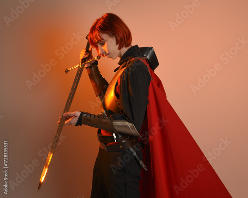portrait of Fantasy warrior woman model, holding sword weapon, historical medieval armour costume with red fairytale cloak, strong fantasy knight. isolated studio background golden cinematic lighting.
