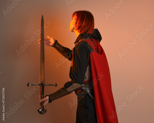 portrait of Fantasy warrior woman model, holding sword weapon, historical medieval armour costume with red fairytale cloak, strong fantasy knight. isolated studio background golden cinematic lighting.