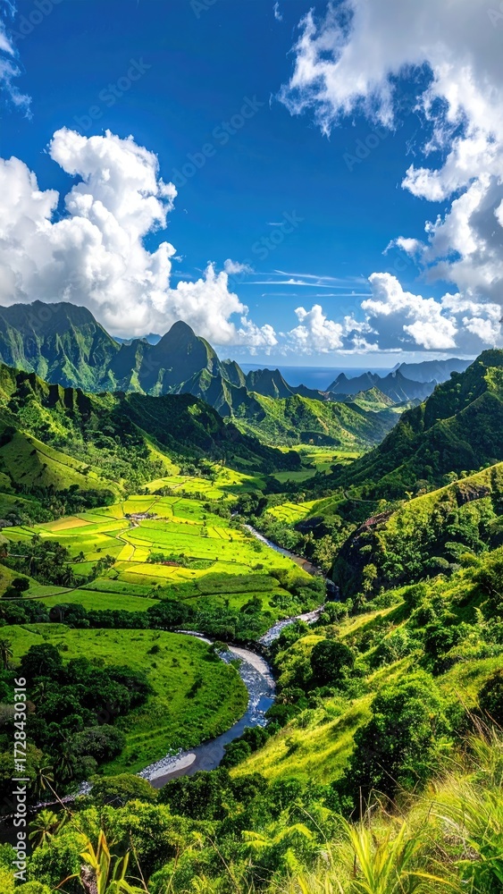 Naklejka premium Lush green valley, river meandering through verdant rice paddies, mountains under a vibrant blue sky with fluffy white clouds