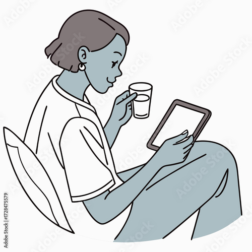 A relaxed young woman with short hair sits comfortably holding a tablet and a glass of water enjoying a moment of leisure and digital engagement