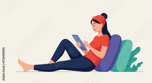 A young woman in a red beanie and t shirt uses a tablet while relaxing on pillows.
