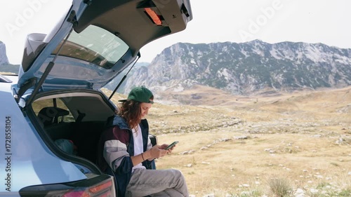 Wallpaper Mural A young woman uses a smartphone while sitting in the trunk of her car with a stunning view of the mountains Torontodigital.ca