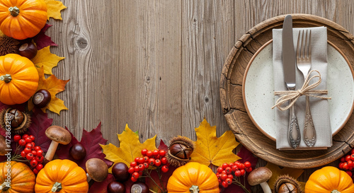 Autumnal table setting on wood background, featuring pumpkins, leaves, chestnuts, and place setting with cutleryÂ Showcases Thanksgiving or fall harvest theme, ideal for seasonal promotions