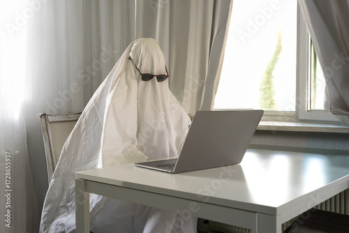 White sheet ghost looking lost at the laptop while working from grey room home office