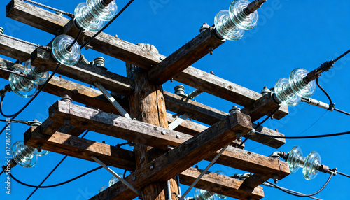 Rustic wooden electricity pole with power lines and glass insulators against a clear blue sky. Concept for energy, electricity, connection, power grid, communication, and infrastructure.