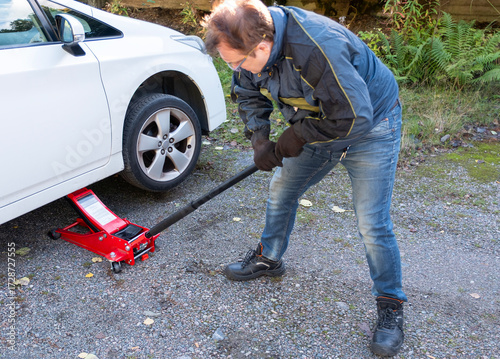 A man jacks up a passenger car for repairs on the street.