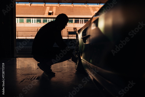 A racing team mechanic prepares a car for competition by checking the tire pressure.