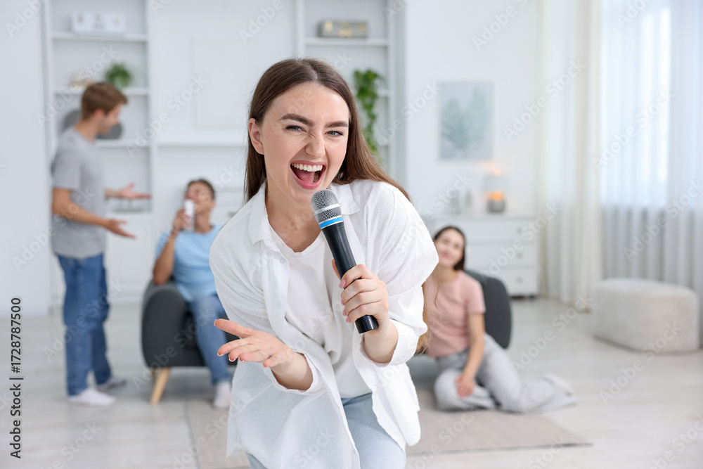 Fototapeta premium Young woman singing karaoke with friends at home, selective focus