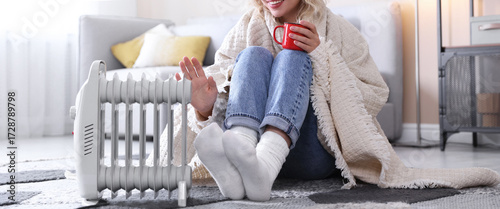 Obraz na plátně Young woman with cup of drink near electric heater on floor at home, closeup