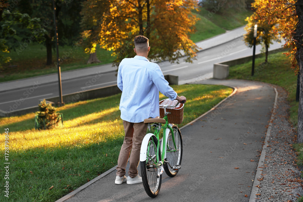 Fototapeta premium Happy man walking his bicycle in park on sunny day, back view