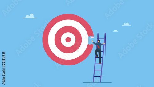 Businessman on ladder using paint roller to paint big dartboard, archery target. Purpose, set business goal or target, KPI, key performance indicator or set objective and achievement.