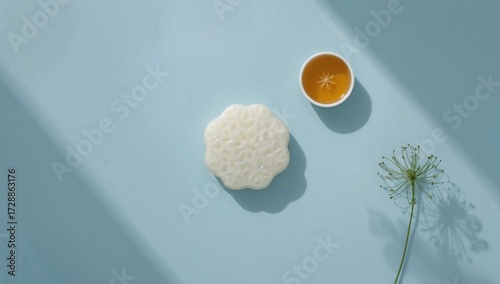 Minimalist overhead shot of a snow skin mooncake with a cup of tea with edible flower garnish, set on a bright blue background with natural light. Flat lay, aesthetic, copy space.