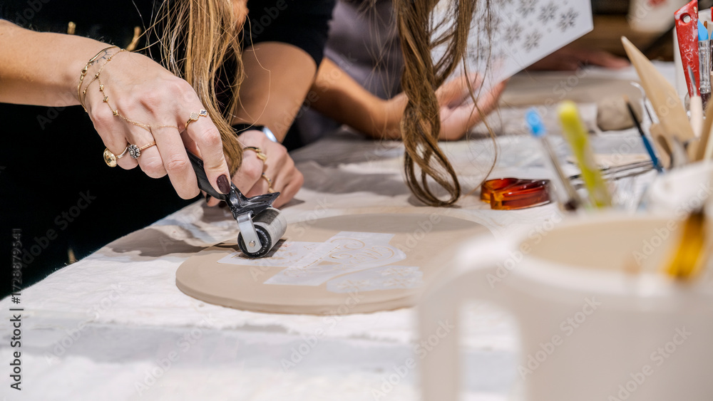Fototapeta premium A woman artist placing a stencil on clay and rolling over it with a cylindrical tool in an art studio