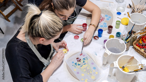 In an art studio during an event, a mother and her young daughter are enjoying quality time together while learning clay shaping as a hobby
