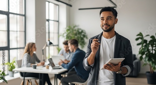 A confident professional holds a tablet while colleagues collaborate in a modern, sunlit office, embodying business success and teamwork