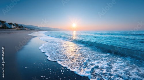 Scenic Sunset Seascape with Blue Ocean Waves Crashing on Dark Sand Beach with Horizon Sunlight Glow and Dramatic Cloudscape at Dusk