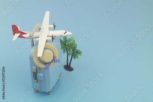 Travel suitcase with beach hat, coconut palm and airplane model on blue background. Copy space for text. Airplane tickets, vacation and travel concept.