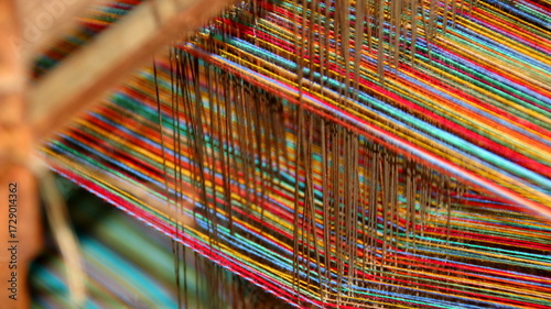 Colorful threads stretch tautly across a wooden loom in a textile workshop, showcasing the intricate process of weaving with vibrant hues and textures.
