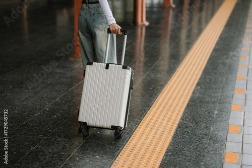 Stylish young woman traveling at train station with suitcase, traveling alone on vacation or business trip, enjoying summer city adventure.