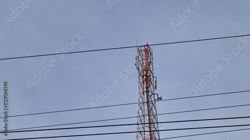 Tall cell tower transmitting signals against a clear blue sky with power lines in the foreground, symbolizing modern communication and connectivity.