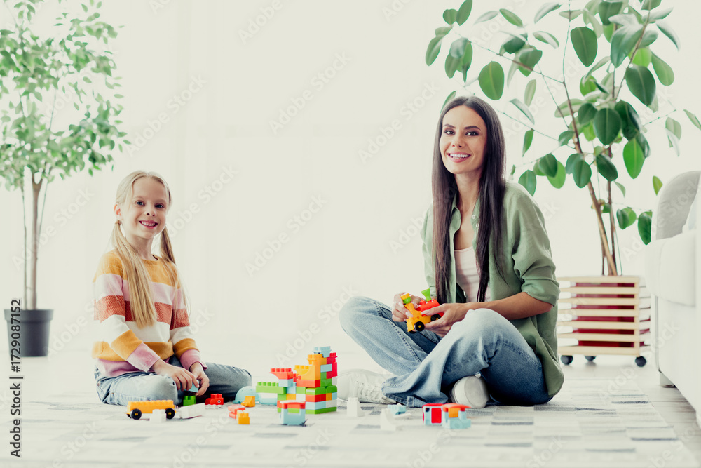 Naklejka premium Mother and daughter playing together with building blocks in a cozy living room, expressing family bonding and fun