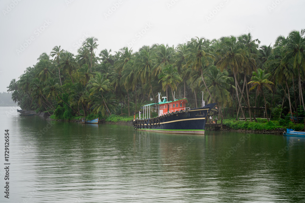 Naklejka premium blue deep water fishing boats with the poles and harnesses parked on a riverside jetty in the backwaters during a rain shower