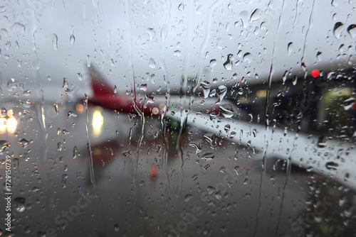 Blurred view to air field with aircrafts through wet glass in the overcast weather in the evening