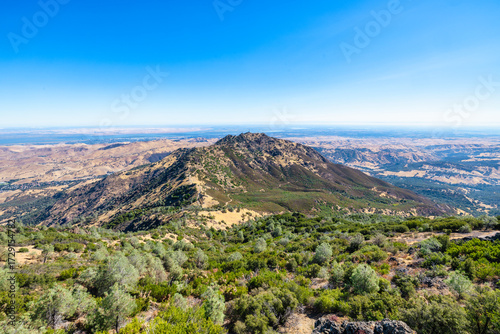 Scenic panorama from Mount Diablo summit in California showing rolling hills, dry golden slopes, green vegetation and clouds drifting over the East Bay landscape under a bright clear blue sky