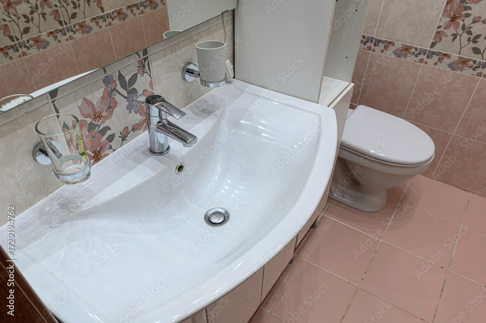 Fototapeta premium A clean bathroom sink with a chrome faucet and a toilet in the background