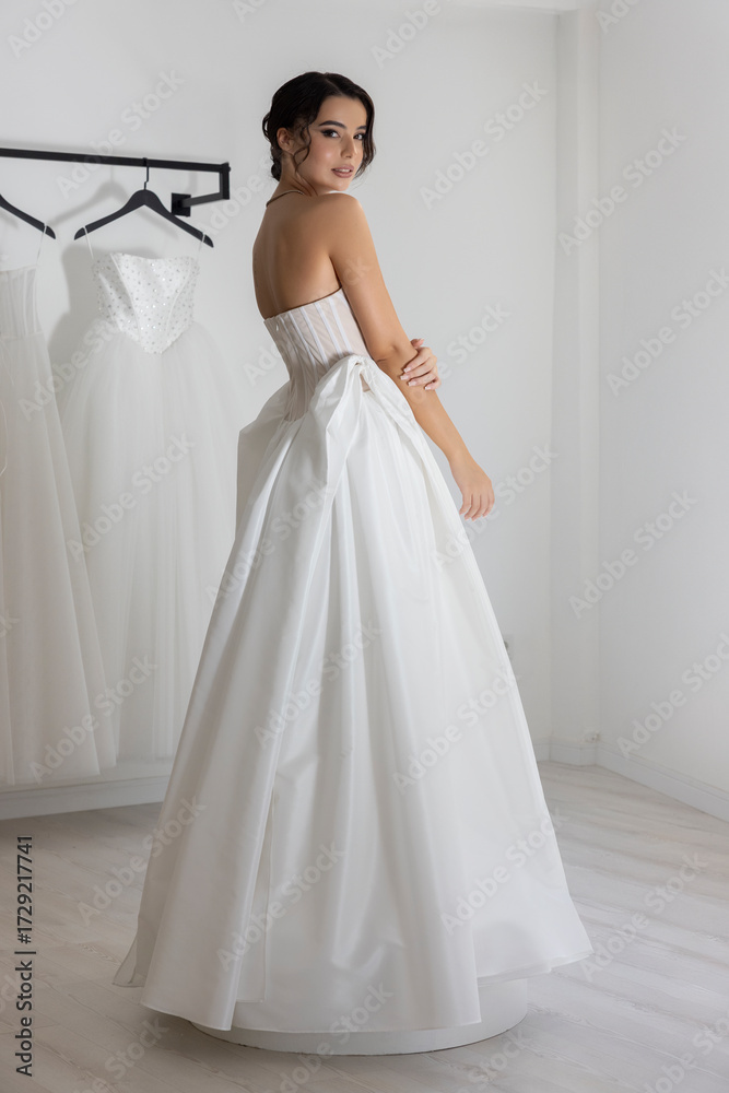 Fototapeta premium Beautiful young woman in strapless white wedding dress posing in studio