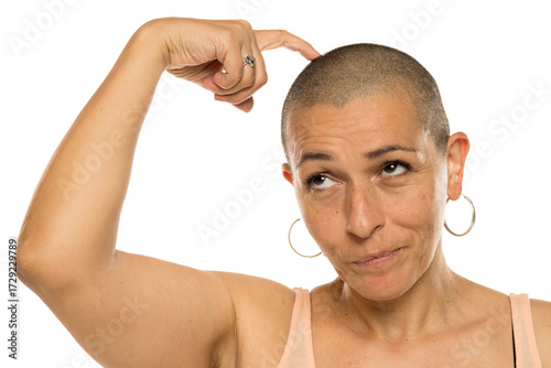 Foto Studio shot of bald woman in light tank top touching head and looking up with thoughtful expression on white background