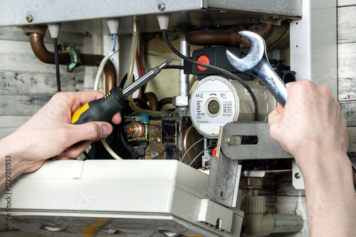 Maintenance of an electric water heating boiler; a man with a wrench and a spanner in his hands is repairing the boiler.