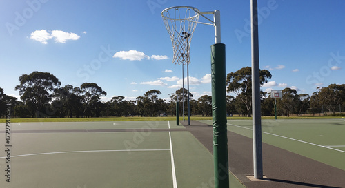 Netball court with hoops and green surroundings under blue sky  