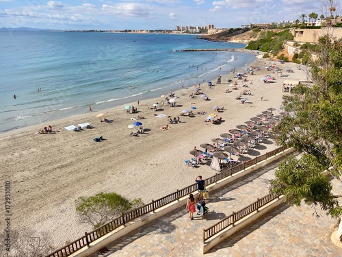 Alicante, Spain - September 24, 2025: Cabo Roig beach scene with sunbathers and umbrellas, showcasing golden sand and tranquil blue waters, perfect for summer relaxation and vacation vibes