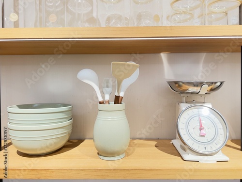 Kitchenware display featuring stacked bowls, cooking utensils in a container, and a vintage scale on a wooden shelf, showcasing culinary organization and style