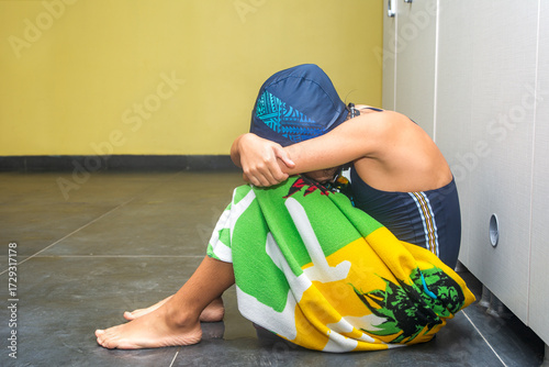 The image of a primary school girl who failed in swimming wrapped in a towel and sat on the floor in the locker room